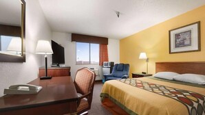 Habitación de hotel con cama, escritorio, silla, televisor y ventana con cortinas.
