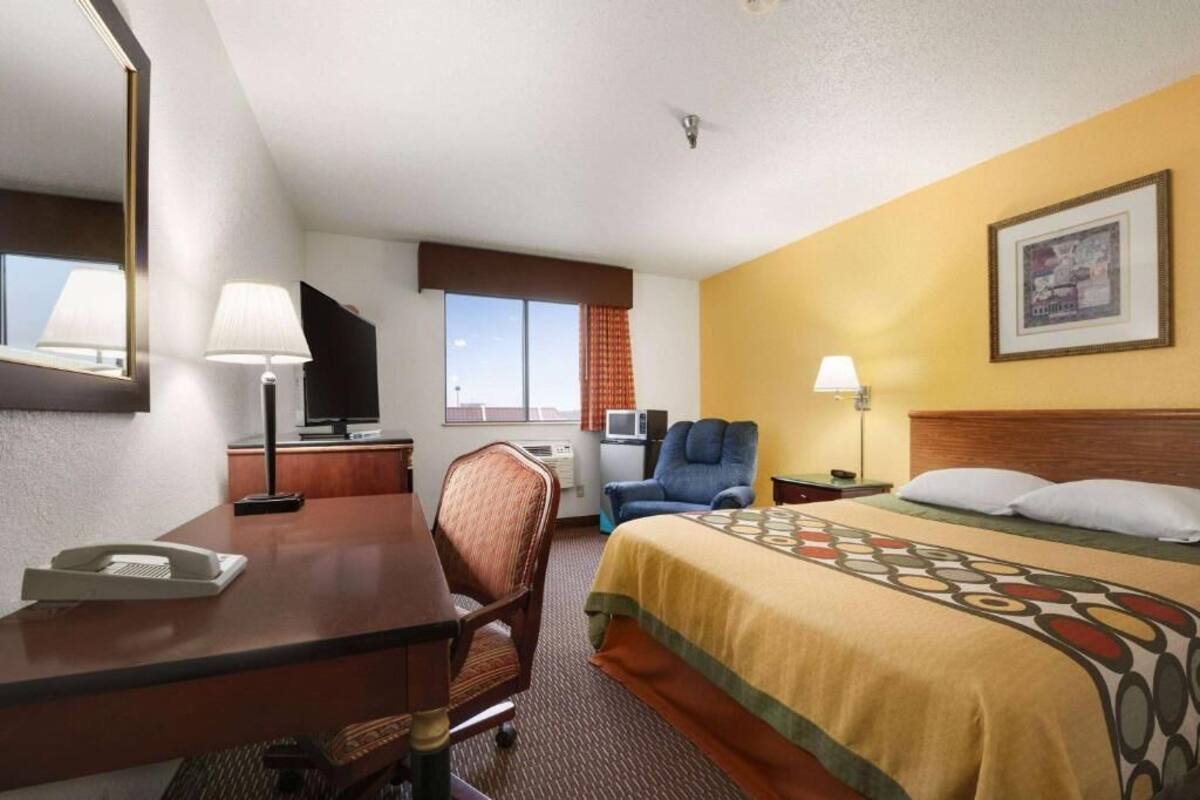 A hotel room with a bed, desk, chair, television, and a window with curtains.