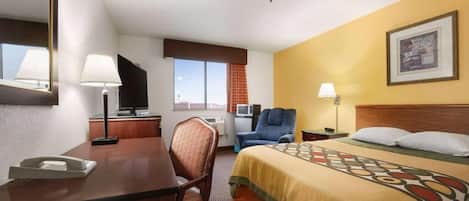 A hotel room with a bed, desk, chair, television, and a window with curtains.