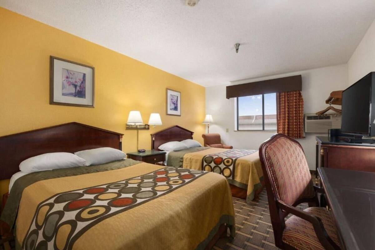 A hotel room with two beds, a desk, a chair, and a television.