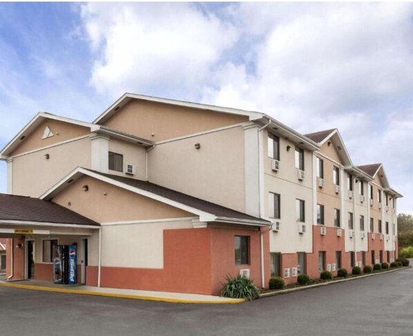 A multi-story hotel with a flat roof, multiple windows, and a parking lot in front.