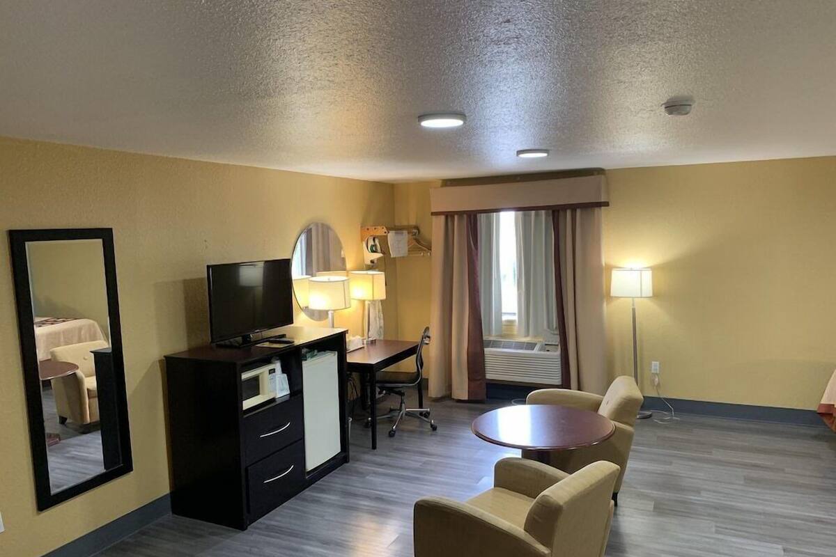 A hotel room with a bed, a desk with a chair, a television, a small table, and a sofa.