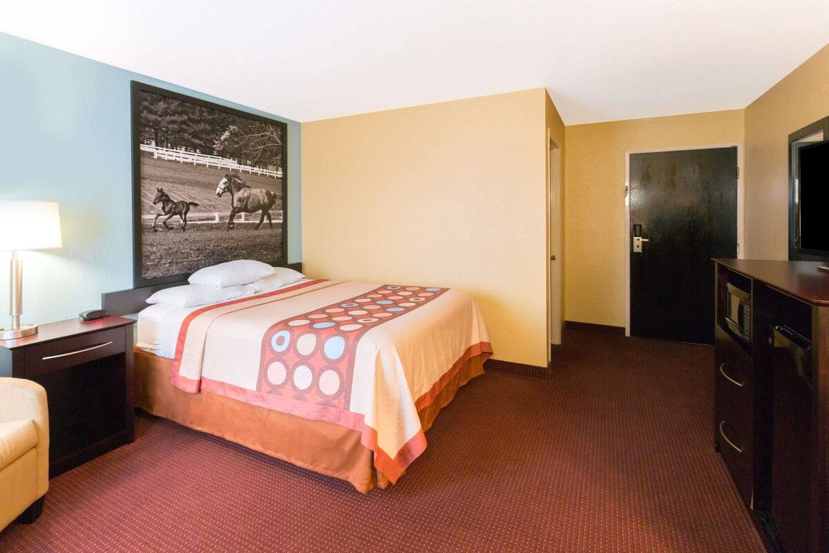 A hotel room with a bed, a nightstand, a lamp, a TV, and a door.