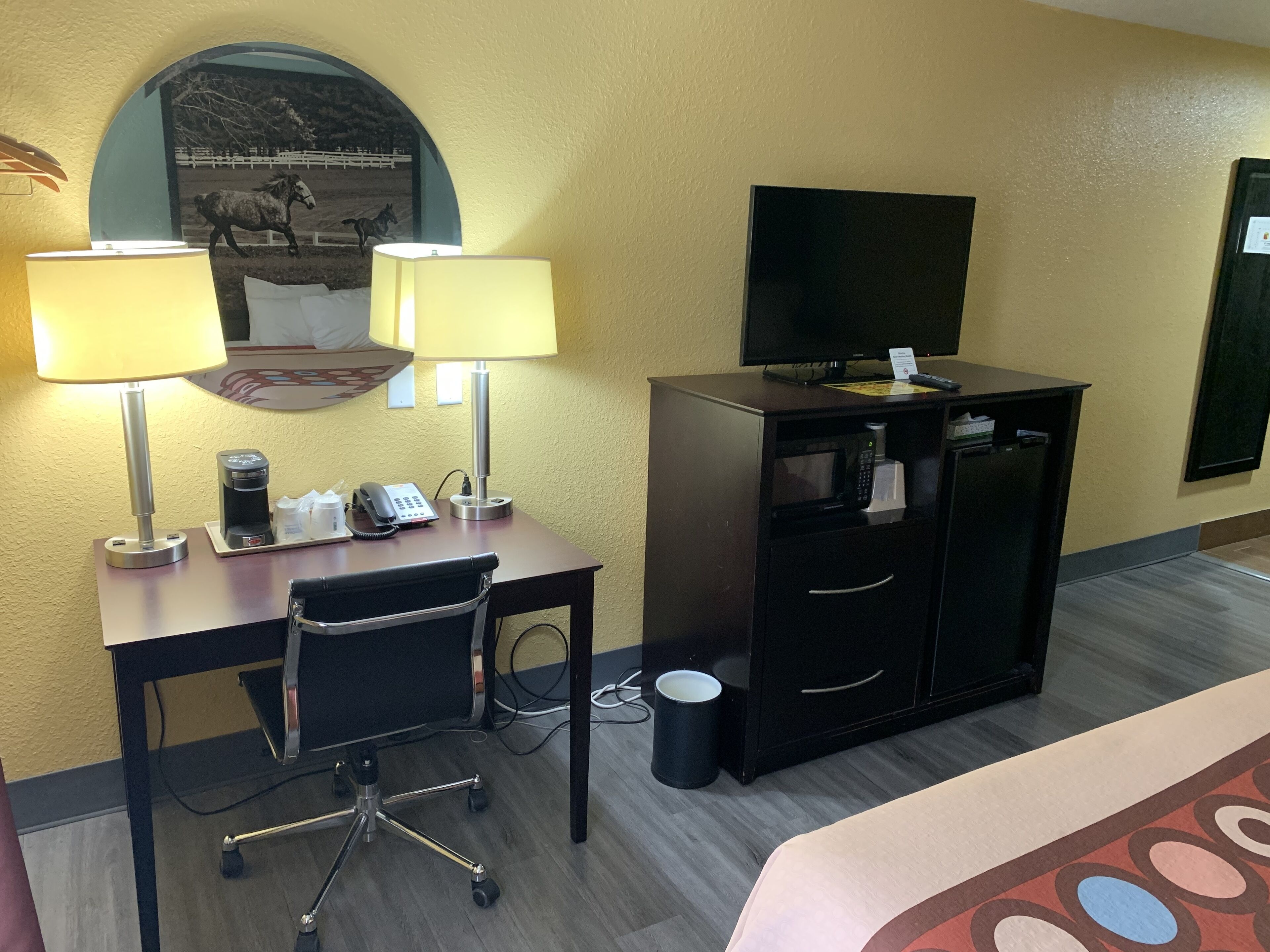 Een hotelkamer met een bureau, twee lampen, een telefoon, koffiezetapparaat, televisie, minibar en een prullenbak.