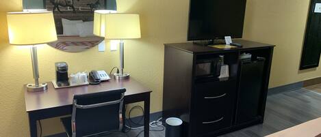 Een hotelkamer met een bureau, twee lampen, een telefoon, koffiezetapparaat, televisie, minibar en een prullenbak.