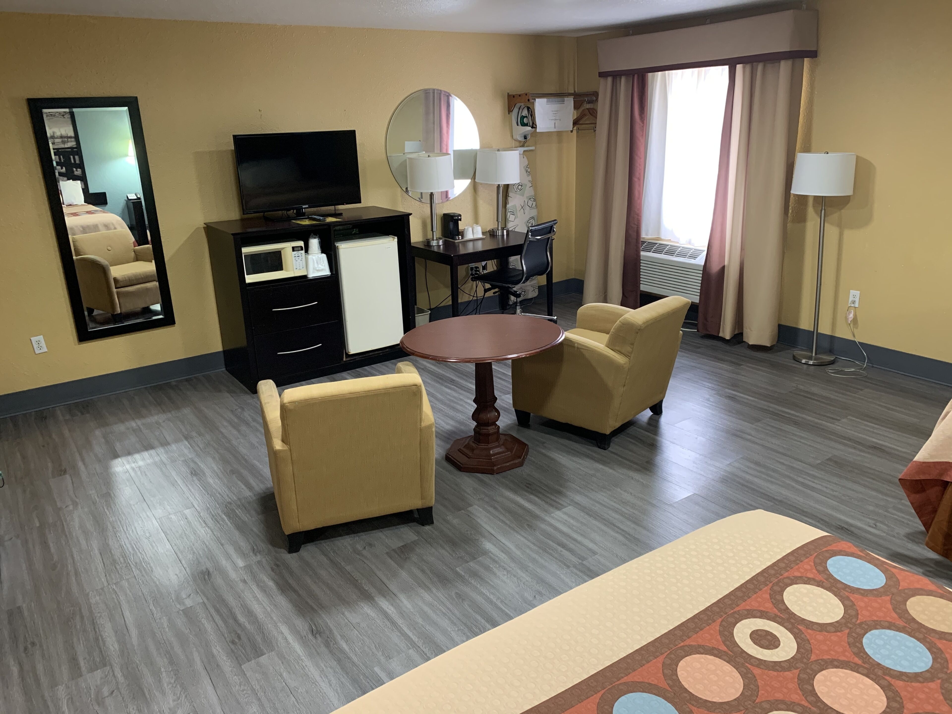 Une chambre d’hôtel comprenant un lit, un bureau avec un ordinateur, une télévision, un miroir, une table à manger avec des chaises et un mini-bar.