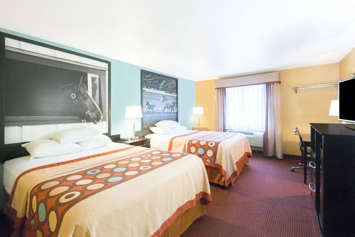 A hotel room with two beds, a desk, a TV, and a window with curtains.