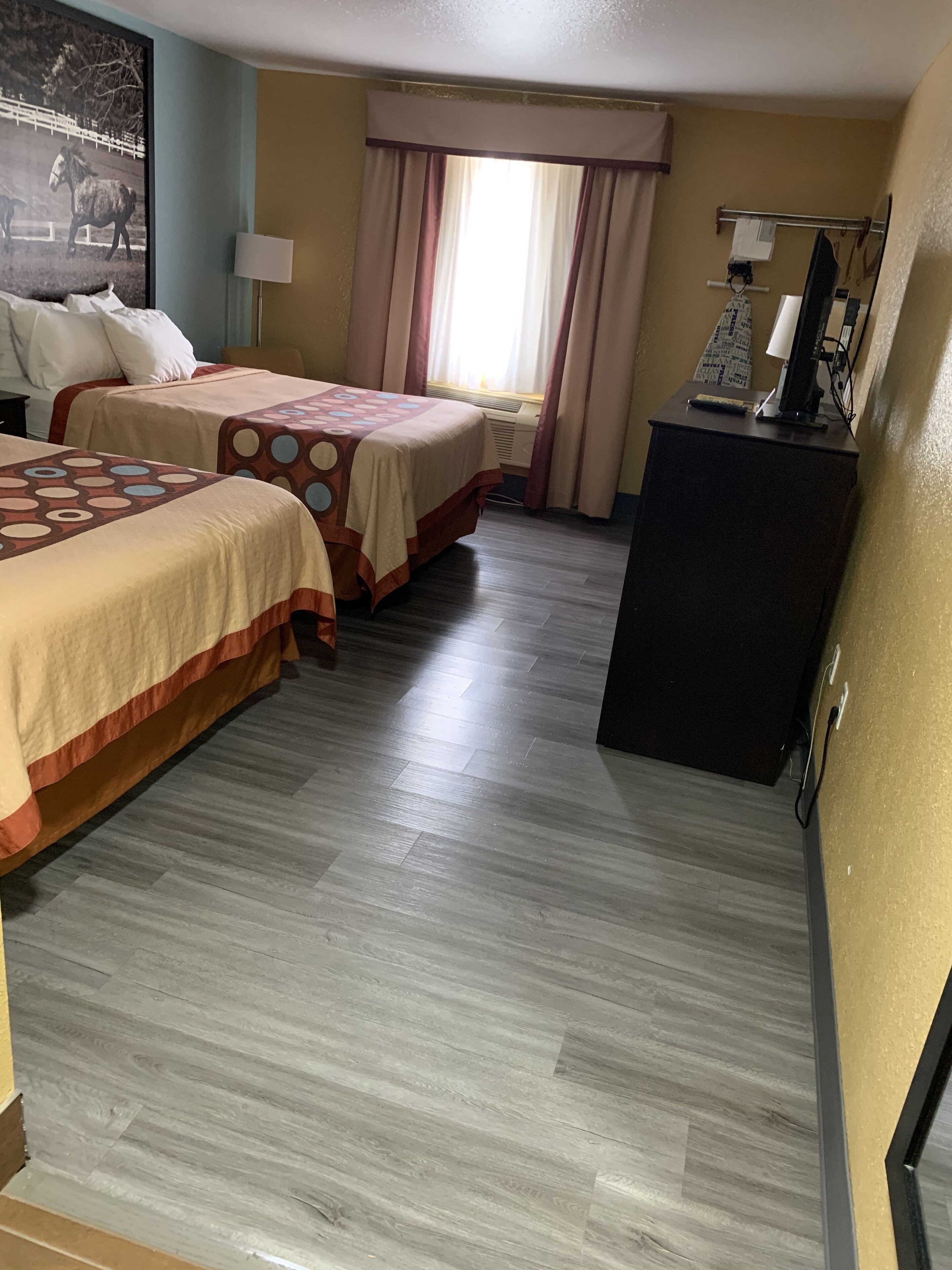 A hotel room with two beds, a desk, a chair, a lamp, and a large window with curtains.