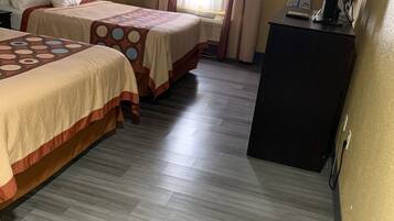 Habitación de hotel con dos camas, un escritorio, una silla, una lámpara y un ventanal con cortinas.