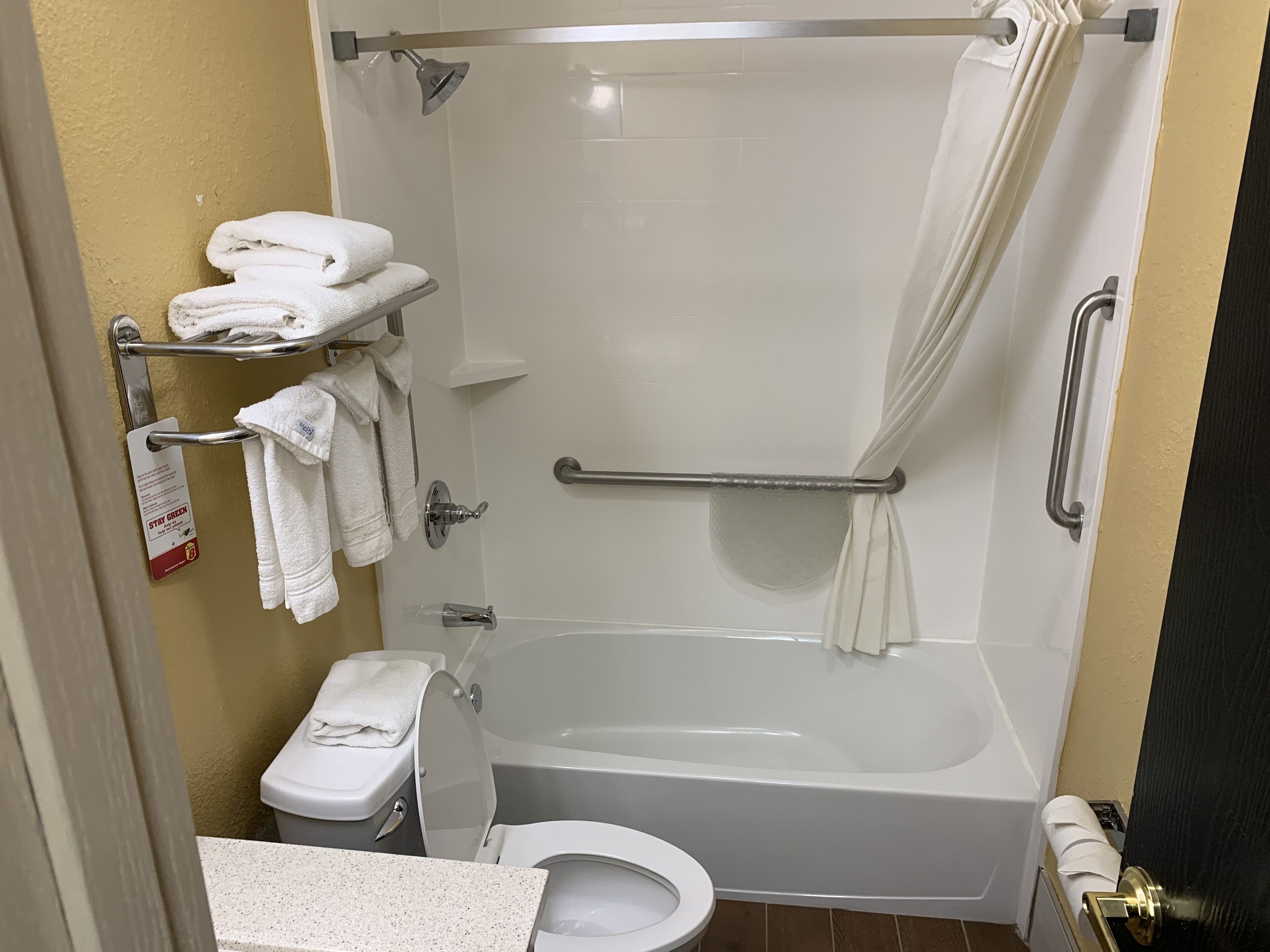 A bathroom with a shower, toilet, and a towel rack with folded towels.