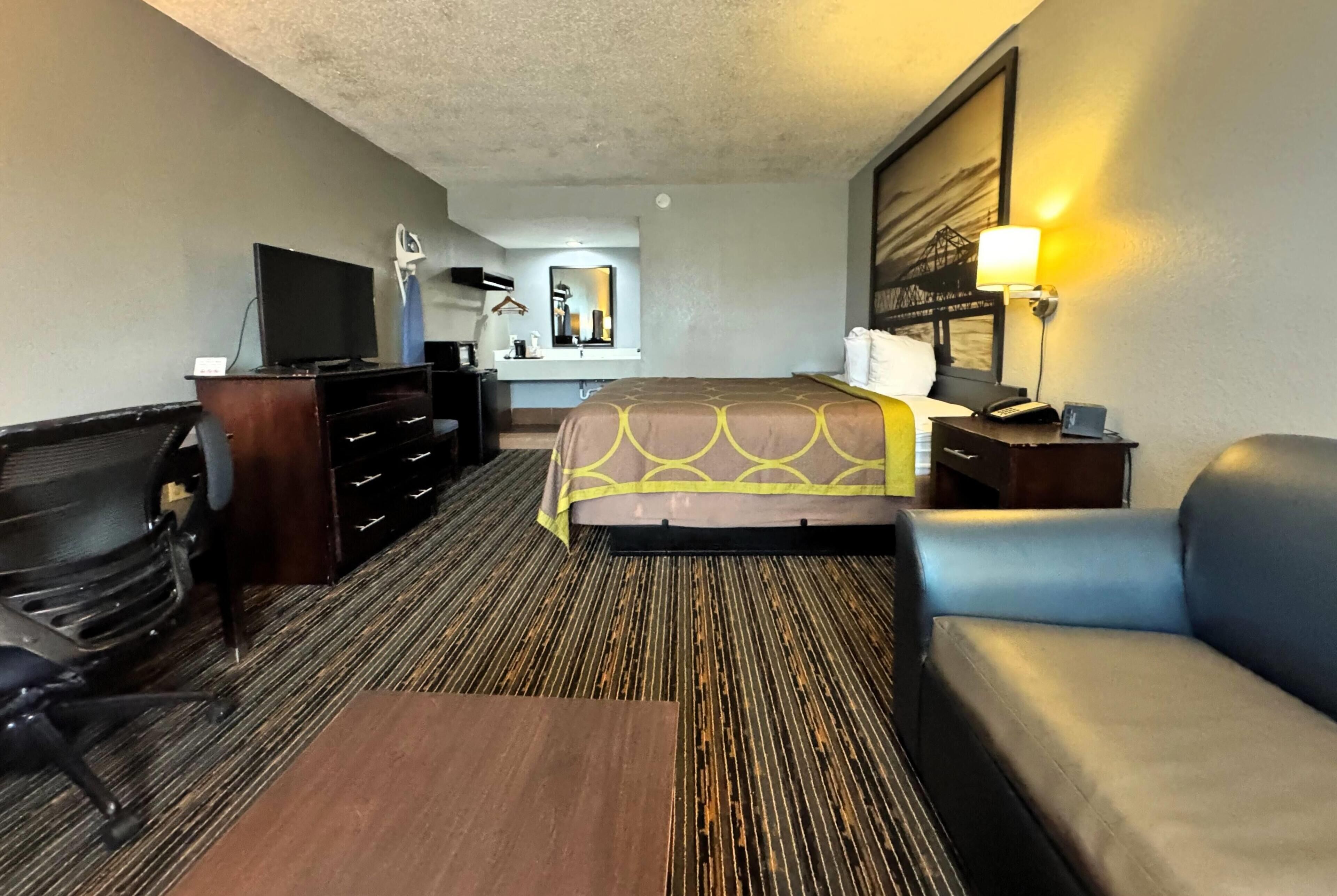 Una habitación de hotel con una cama, un escritorio con computadora, una silla, un televisor y una lámpara.