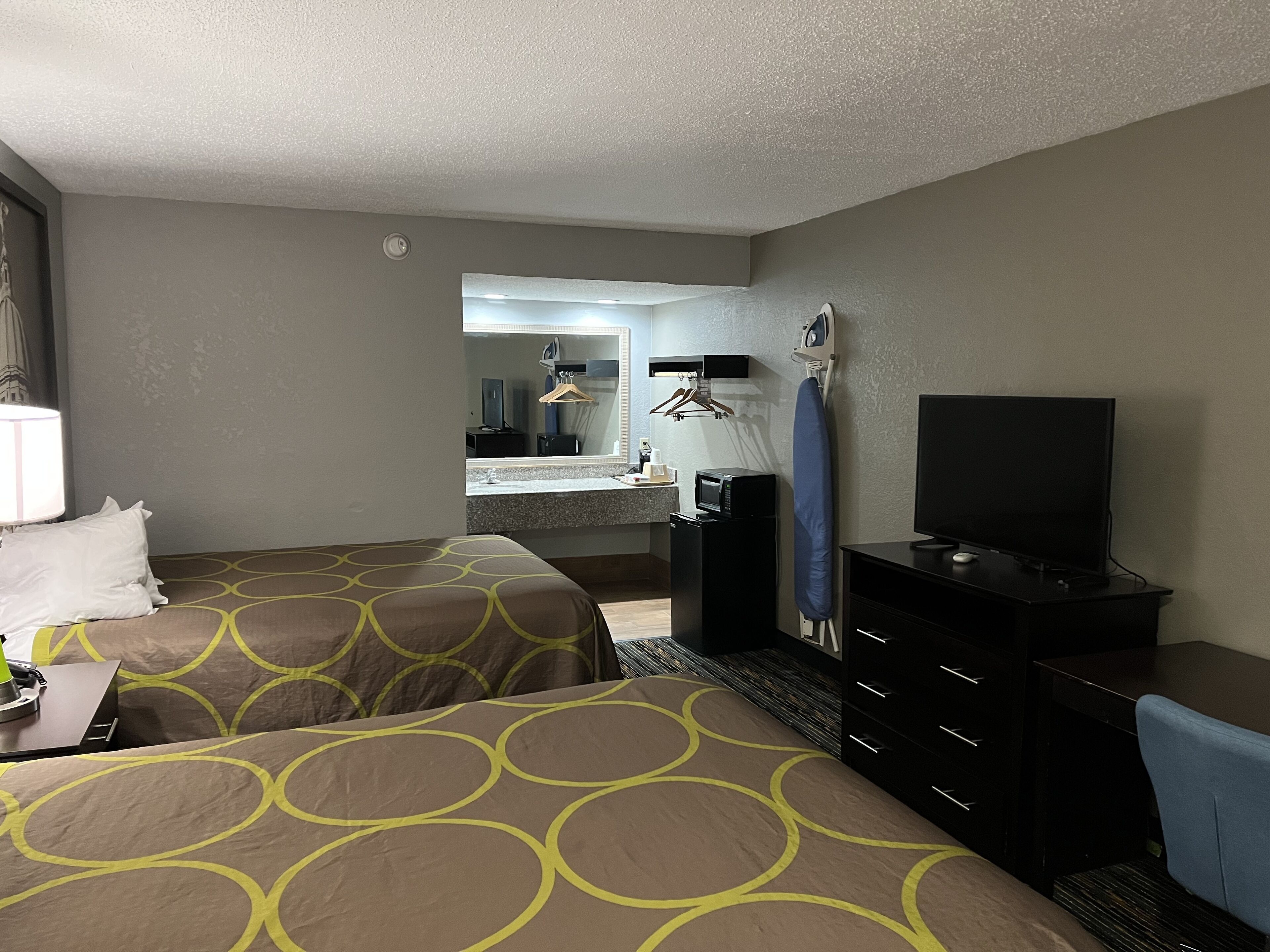 A hotel room with two beds, a desk, a dresser, a television, and a mirror.
