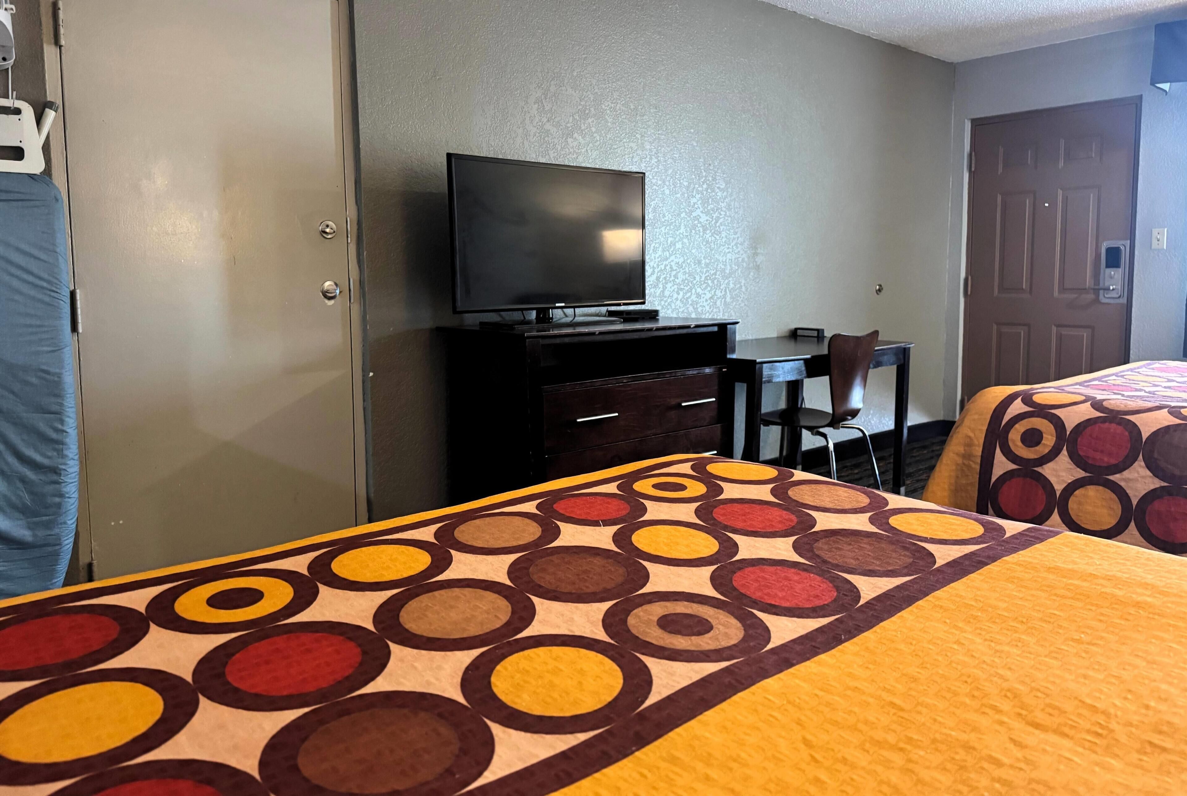 Une chambre d’hôtel avec un lit, un téléviseur posé sur une commode, un bureau avec une chaise et une porte.