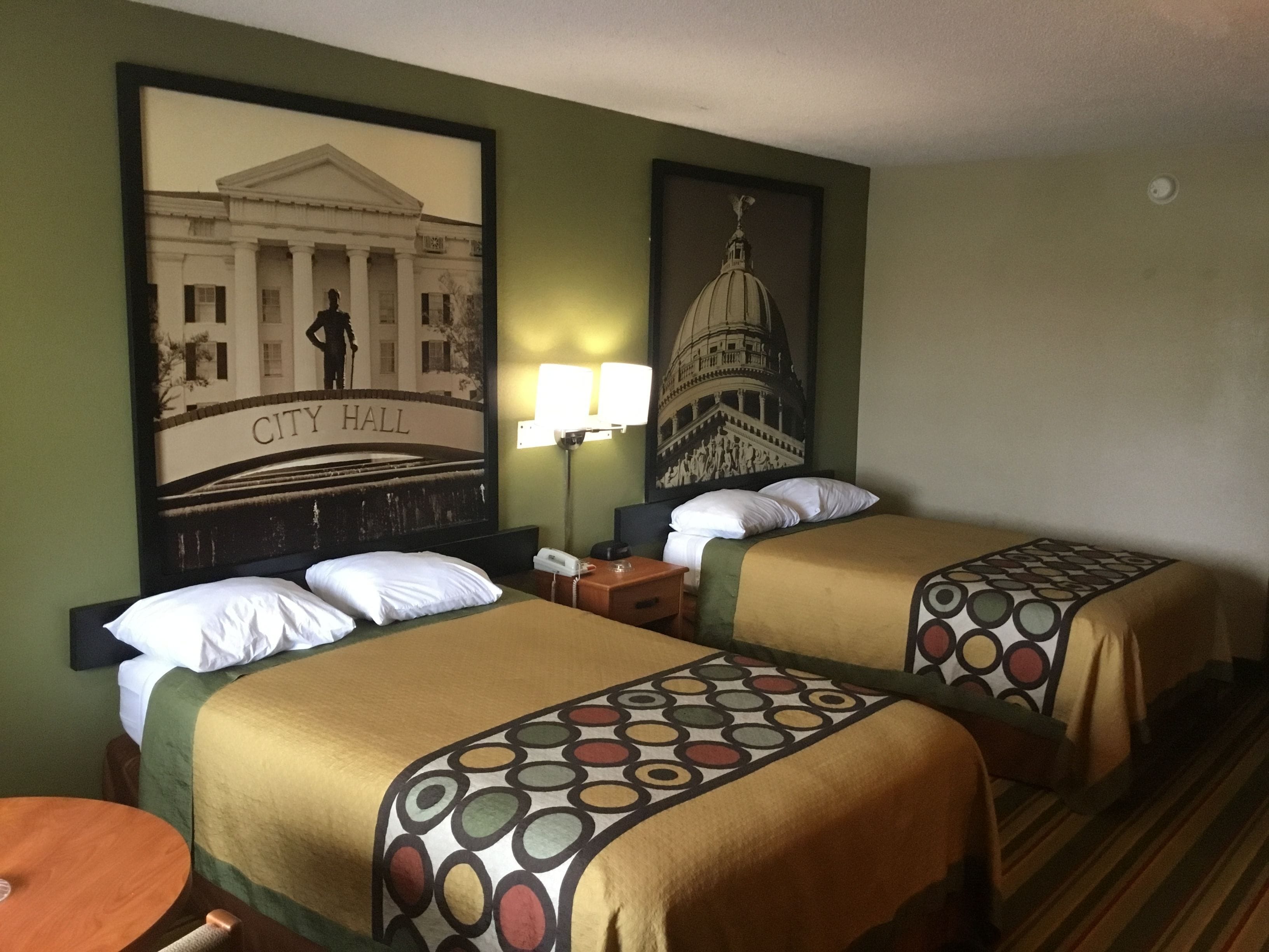 A hotel room with two beds, a nightstand, a lamp, and two framed pictures on the wall.