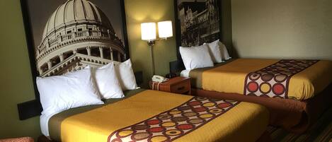 Una habitación de hotel con dos camas, una mesita de noche, una lámpara y una silla.