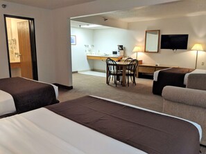 A hotel room with two beds, a desk, a chair, a TV, and a lamp.