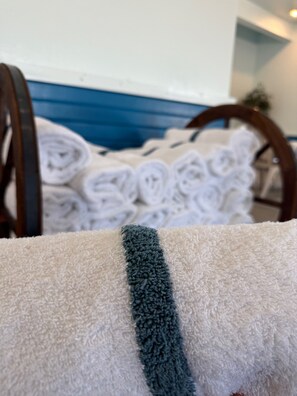 A close-up of a white towel with a dark blue stripe, a wooden bed frame, and a blue wall in the background.