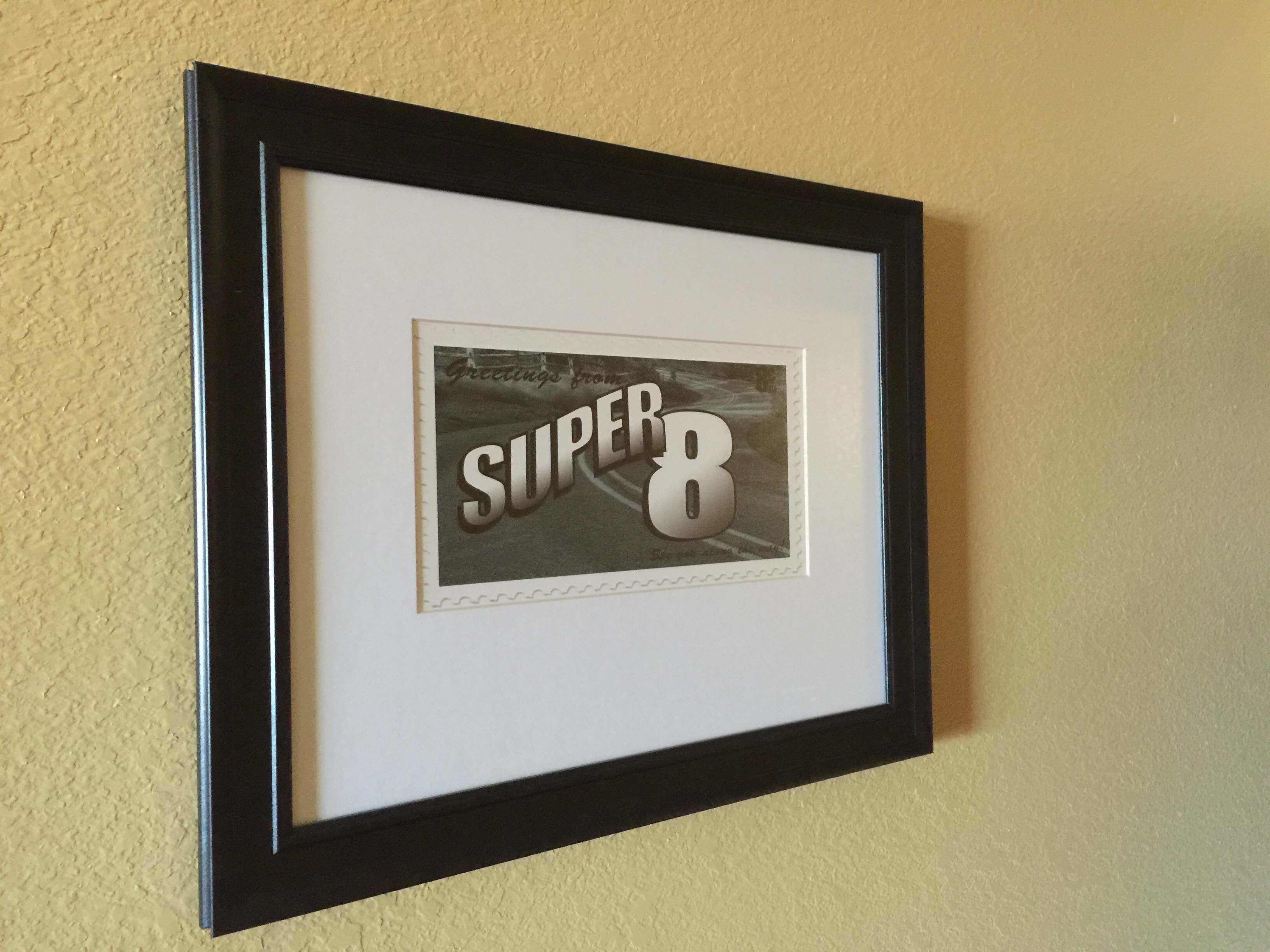 Une photo encadrée avec l’inscription « Salutations de SUPER 8 » sur un mur à texture.