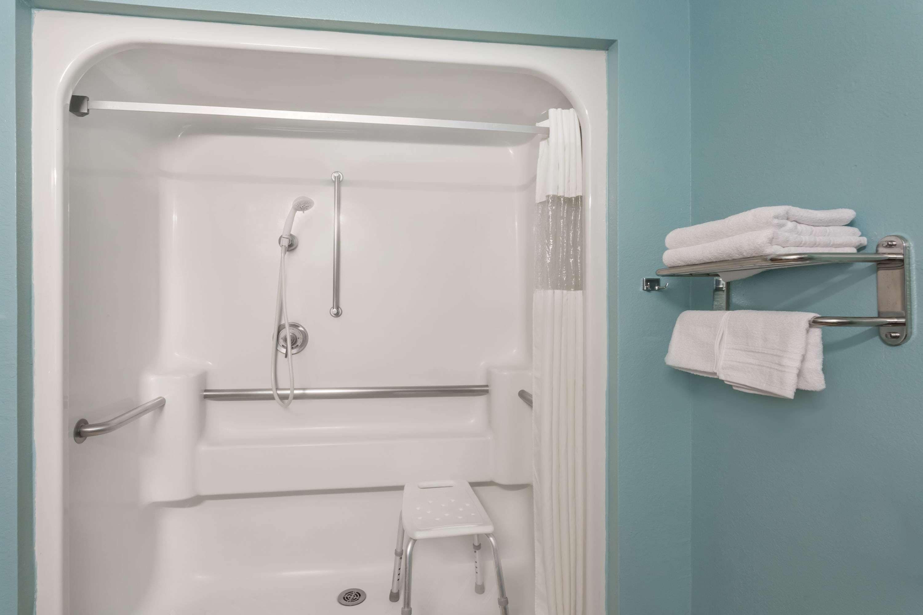 Un baño con bañera, barras de apoyo, un taburete y un perchero para toallas.