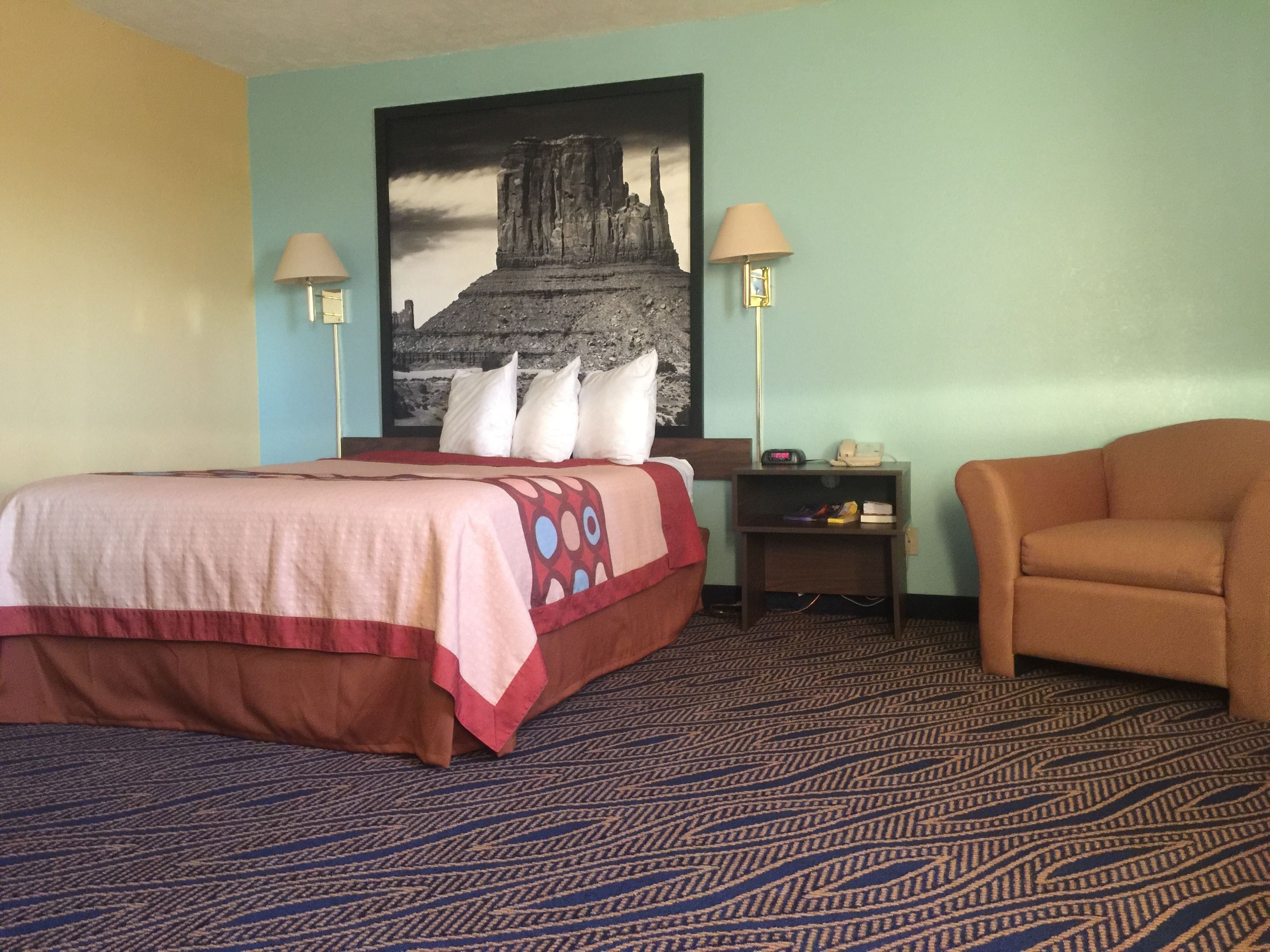 Ein Hotelzimmer mit einem Bett, zwei Nachttischlampen, einem Nachttisch, einem Sessel und einem großen Wandbild.