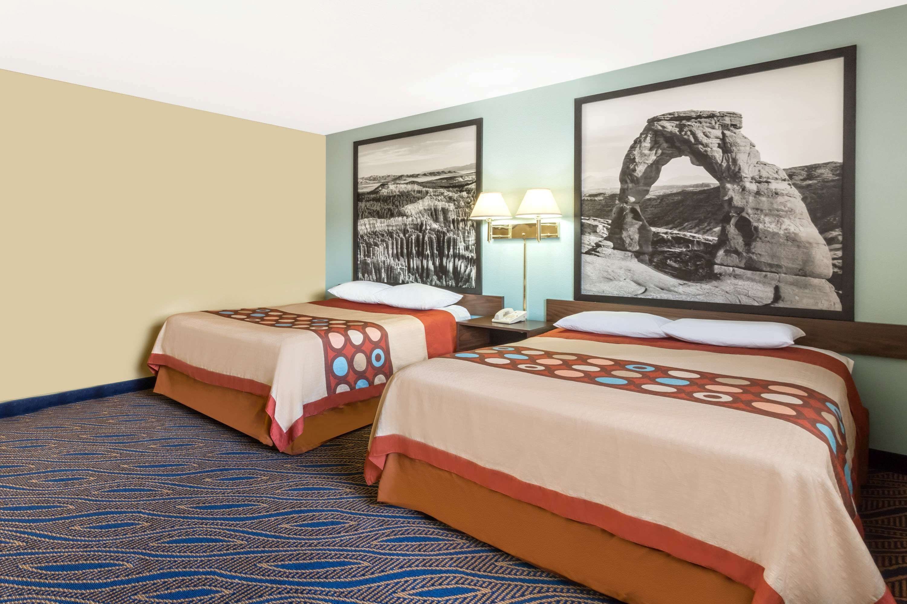 Une chambre d’hôtel avec deux lits, une moquette à motifs et deux photographies encadrées accrochées au mur.