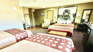 A hotel room with two beds, a desk, a chair, a lamp, and a framed picture on the wall.