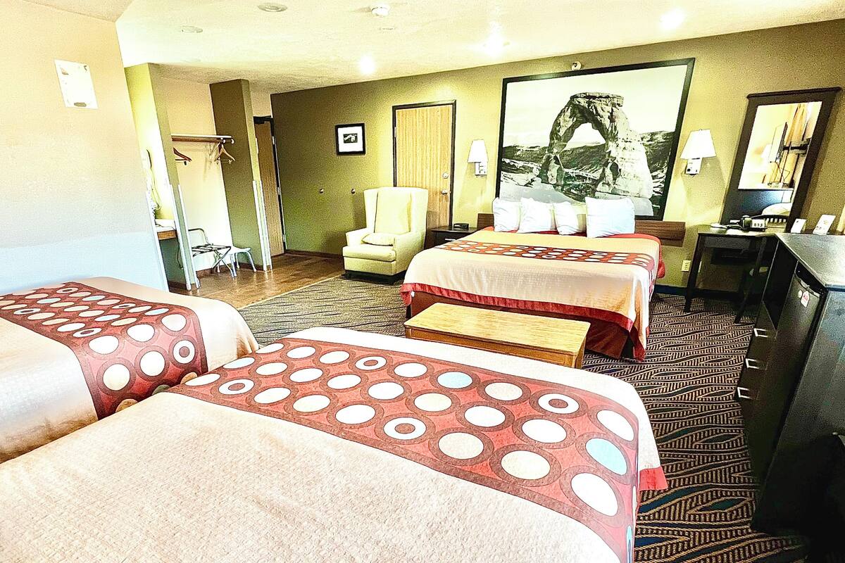 Une chambre d’hôtel avec deux lits, un bureau, une chaise, une lampe et un tableau encadré au mur.