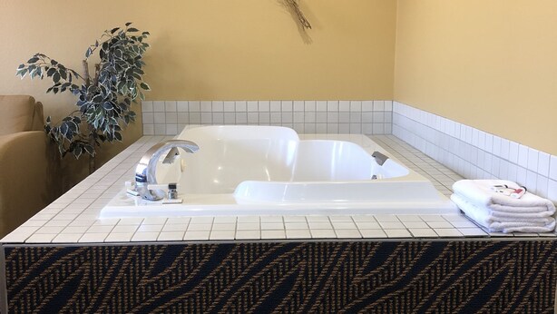 A bathroom with a large bathtub, a potted plant, and a tiled floor.