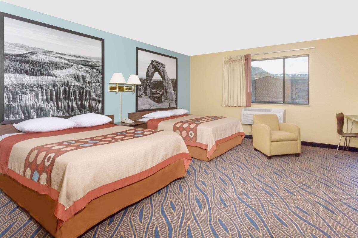 Une chambre d’hôtel avec deux lits, un bureau, une chaise et de grandes peintures représentant des paysages accrochées aux murs.