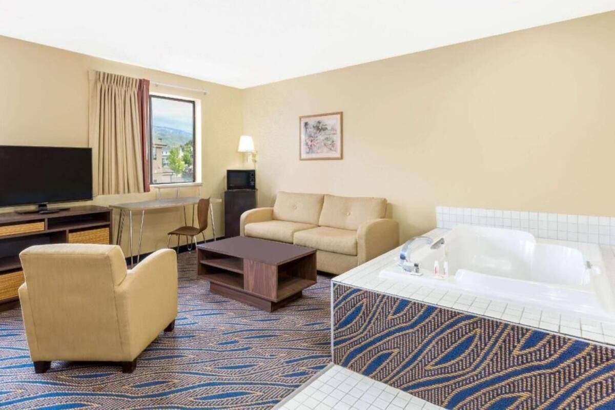 Habitación de hotel con sofá, sillón, televisor de pantalla plana, escritorio, lámpara y bañera.