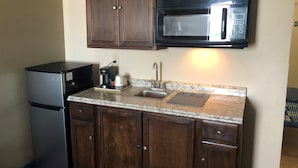 A compact kitchen with a refrigerator, a coffee maker, a microwave, and a sink.