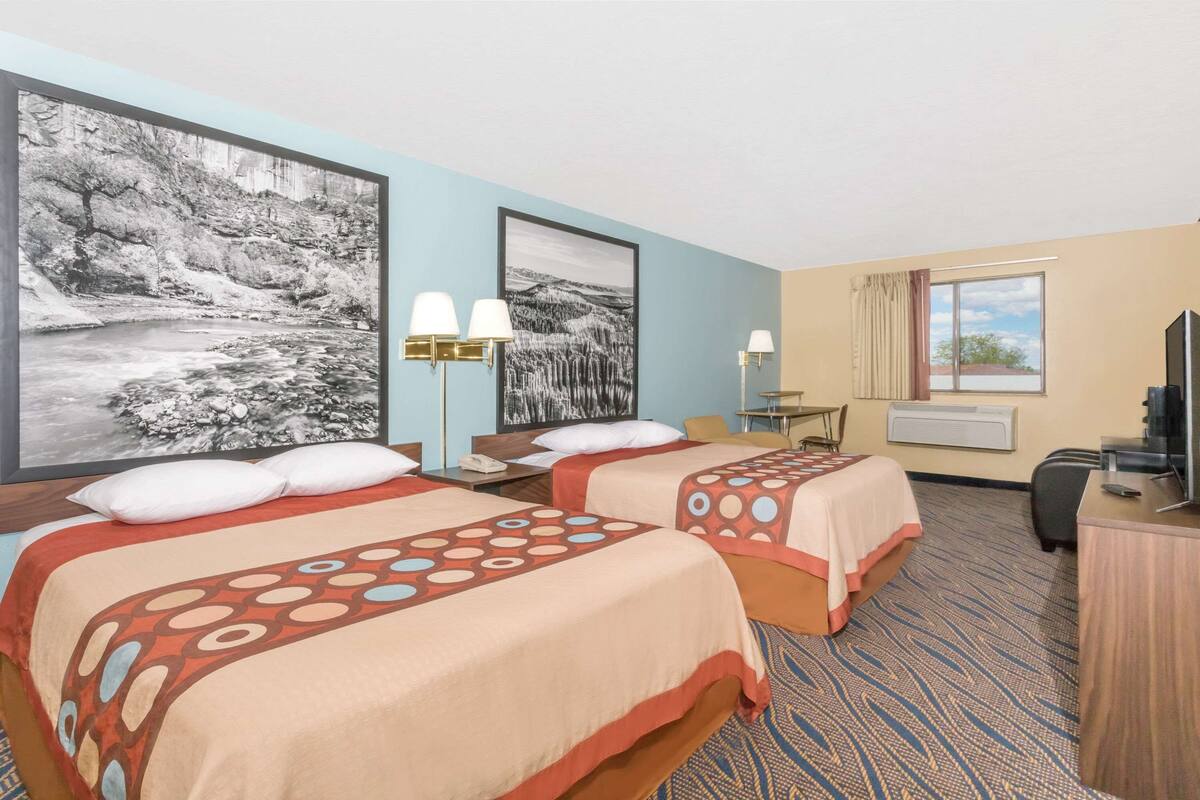 Une chambre d’hôtel avec deux lits, un bureau, une télévision et un grand tableau encadré au mur.