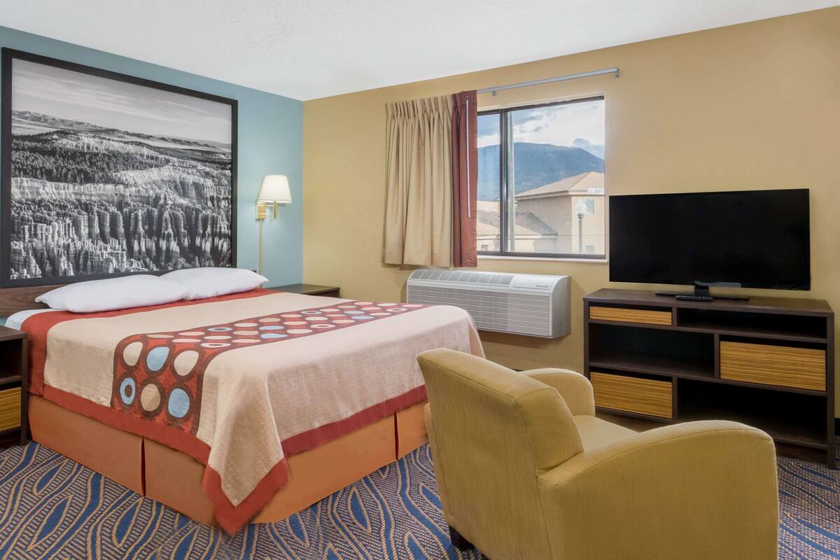 Une chambre d’hôtel avec un lit, une télévision, une chaise et une grande fenêtre.