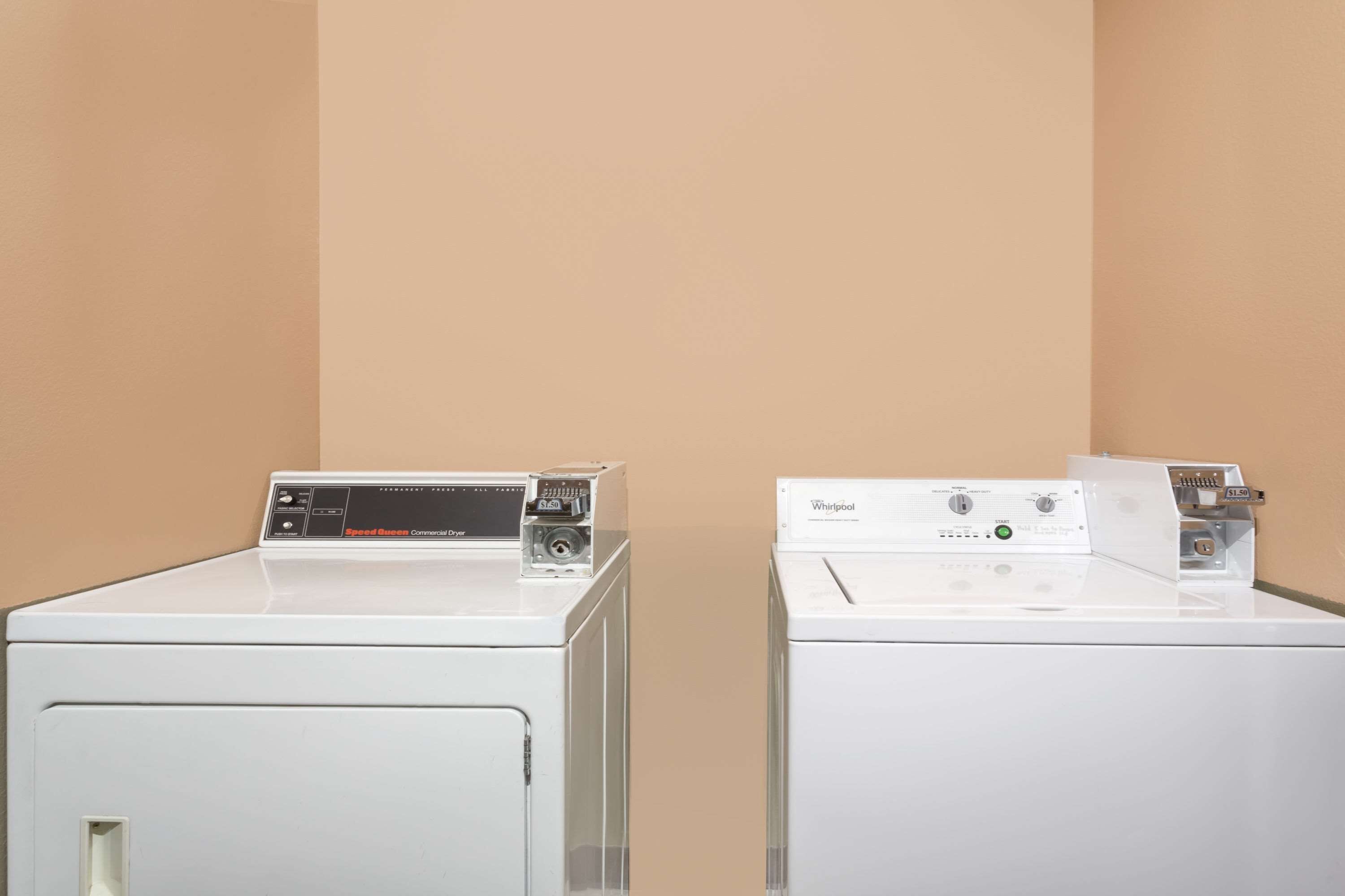 Two white front-loading washing machines in a corner with beige walls.