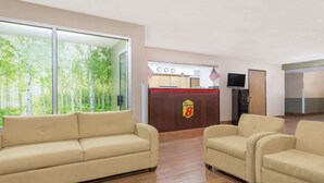 A hotel lobby with a reception desk, American flags, a television, and beige sofas.