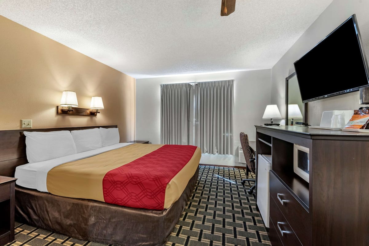 A hotel room with a bed, a desk, a television, and a window with curtains.