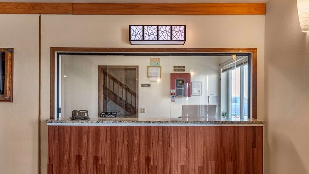 Un mostrador de recepción con diseño de panel de madera, una mampara de vidrio y vistas a una escalera y una máquina expendedora roja.