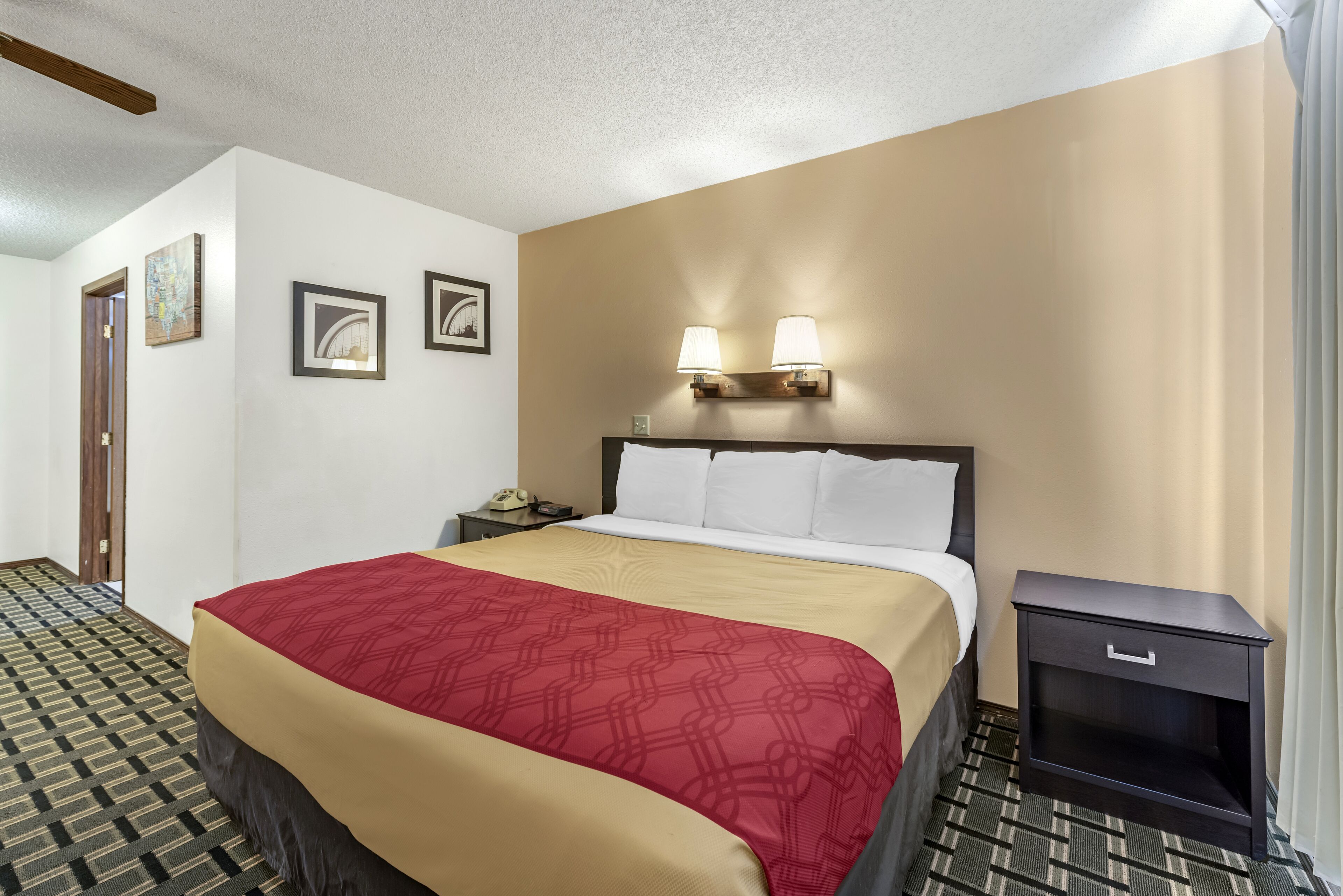 A hotel room with a bed, a nightstand, two wall-mounted lamps, and a patterned carpet.