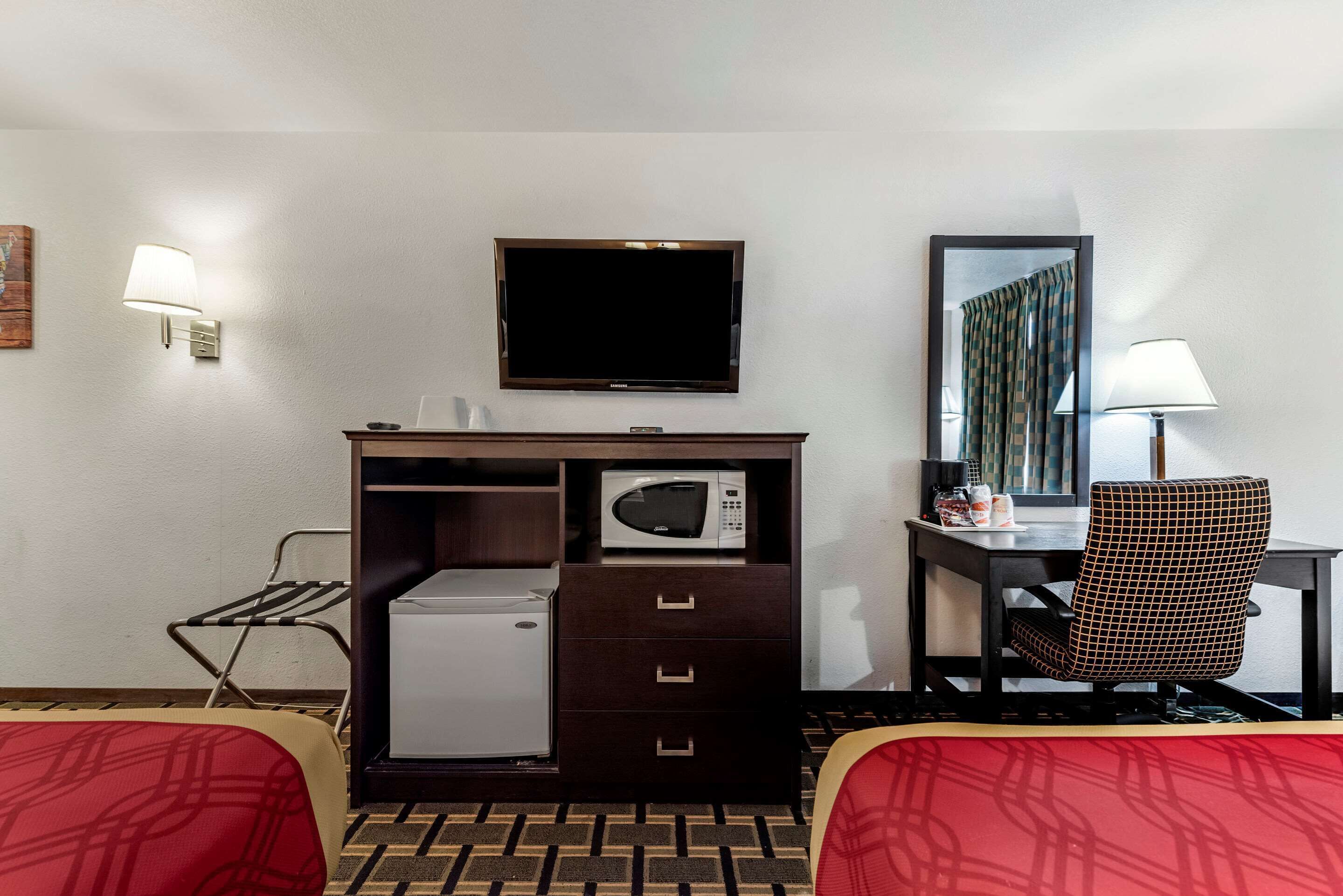 A hotel room with a bed, a desk with a computer, a microwave, a small refrigerator, and a TV.