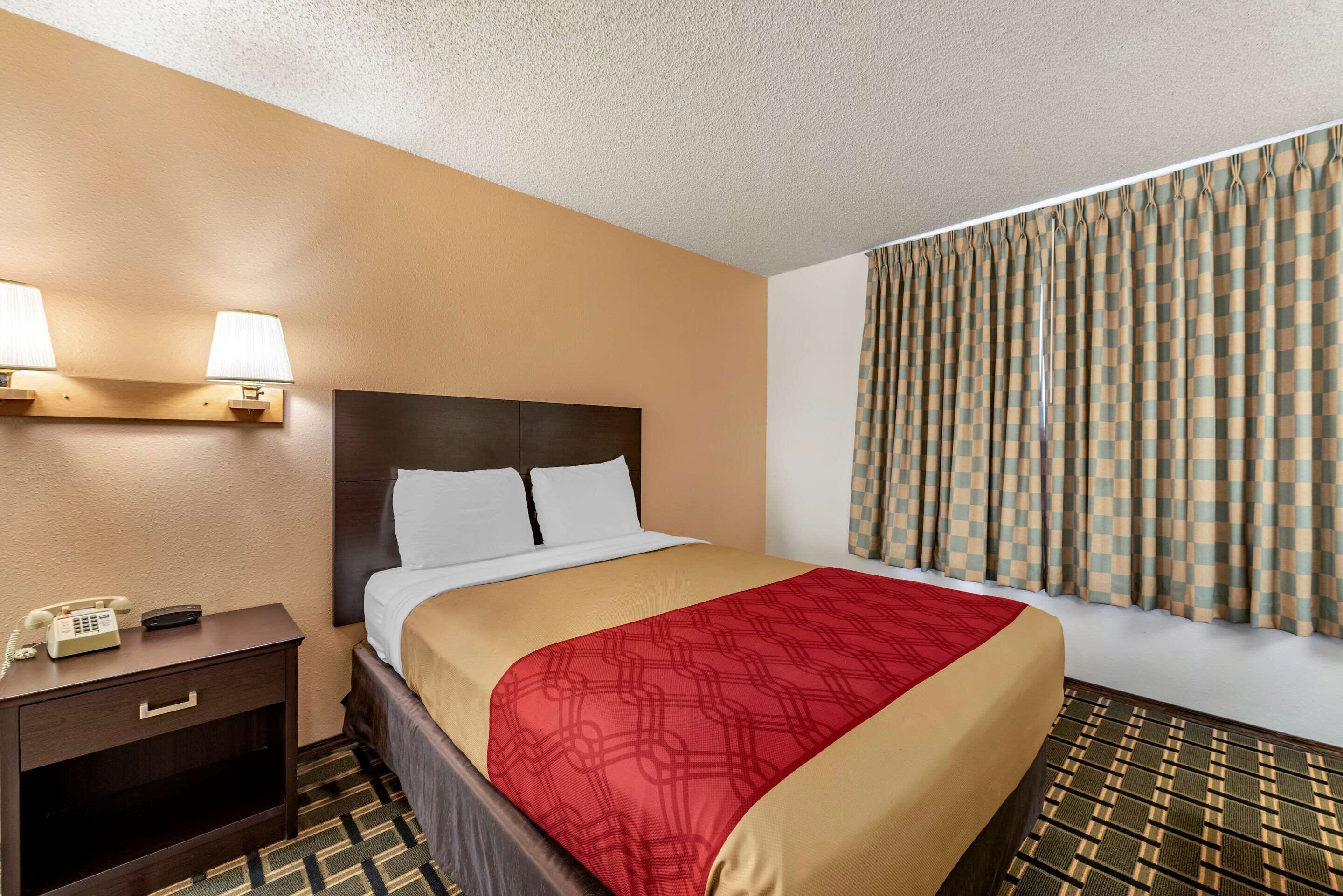 A hotel room with a bed, bedside lamps, a telephone, and a window with curtains.