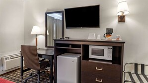 Habitación de hotel con escritorio, silla, mini bar, televisor y microondas.