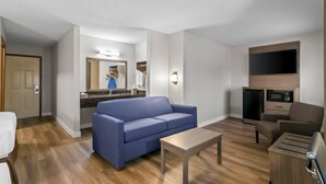 A modern living room with a blue sofa, a wooden coffee table, a TV, and a kitchenette. - Quality Inn Neosho (Neosho)