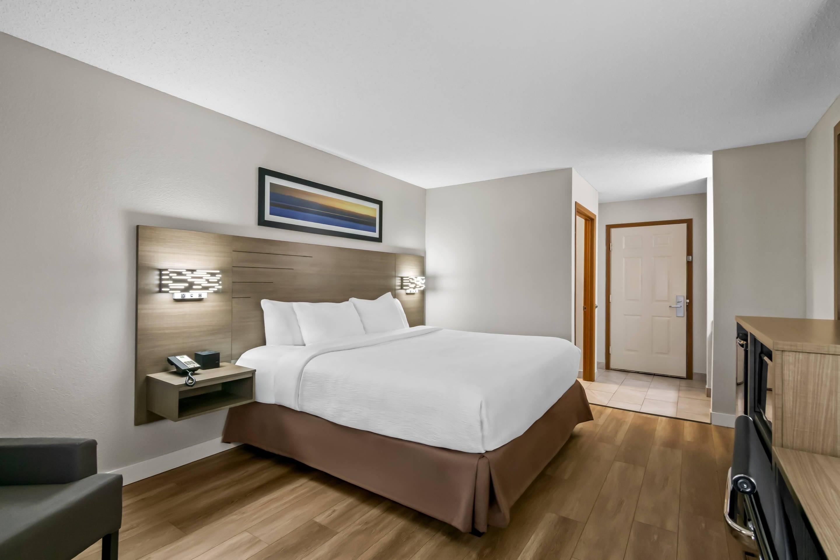 Habitación de hotel moderna con una cama grande, una mesita de noche y una lámpara de pared.