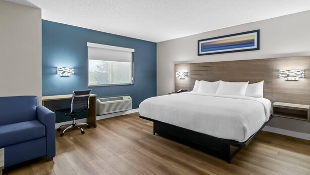 A modern hotel room with a large bed, a desk, a chair, and a window.