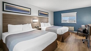 A hotel room with two beds, a desk, a chair, a lamp, and two framed pictures on the wall.