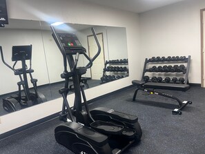 A gym with cardio equipment, dumbbells, and a mirror.