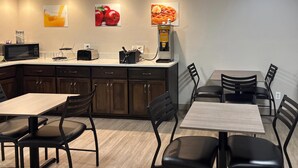 A modern kitchen with a microwave, toaster, and waffle maker on the counter. There are wooden cabinets and a dining area with chairs and tables.