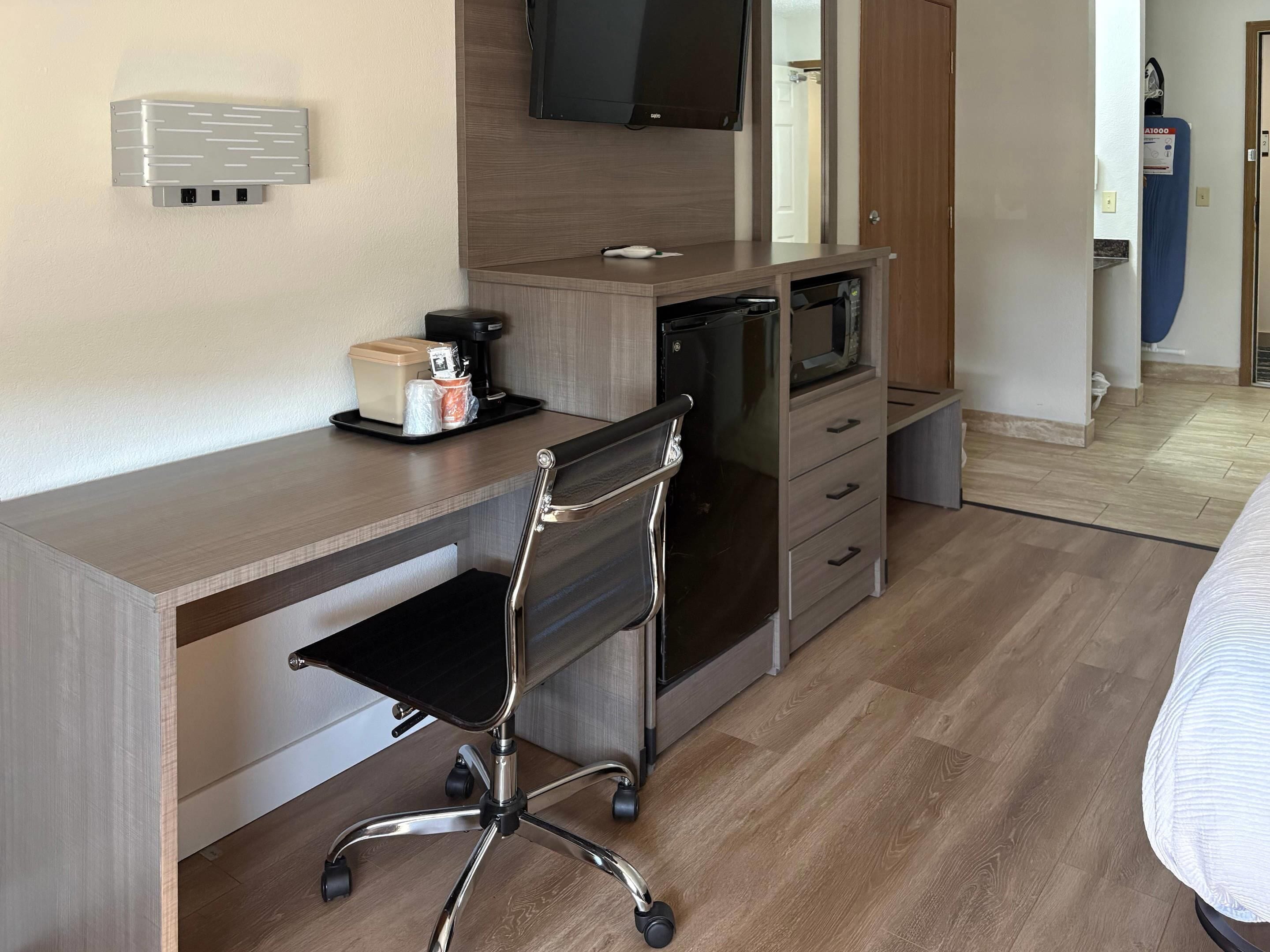Een hotelkamer met een houten bureau, een zwarte bureaustoel, een televisie, een magnetron en een waterdispenser.