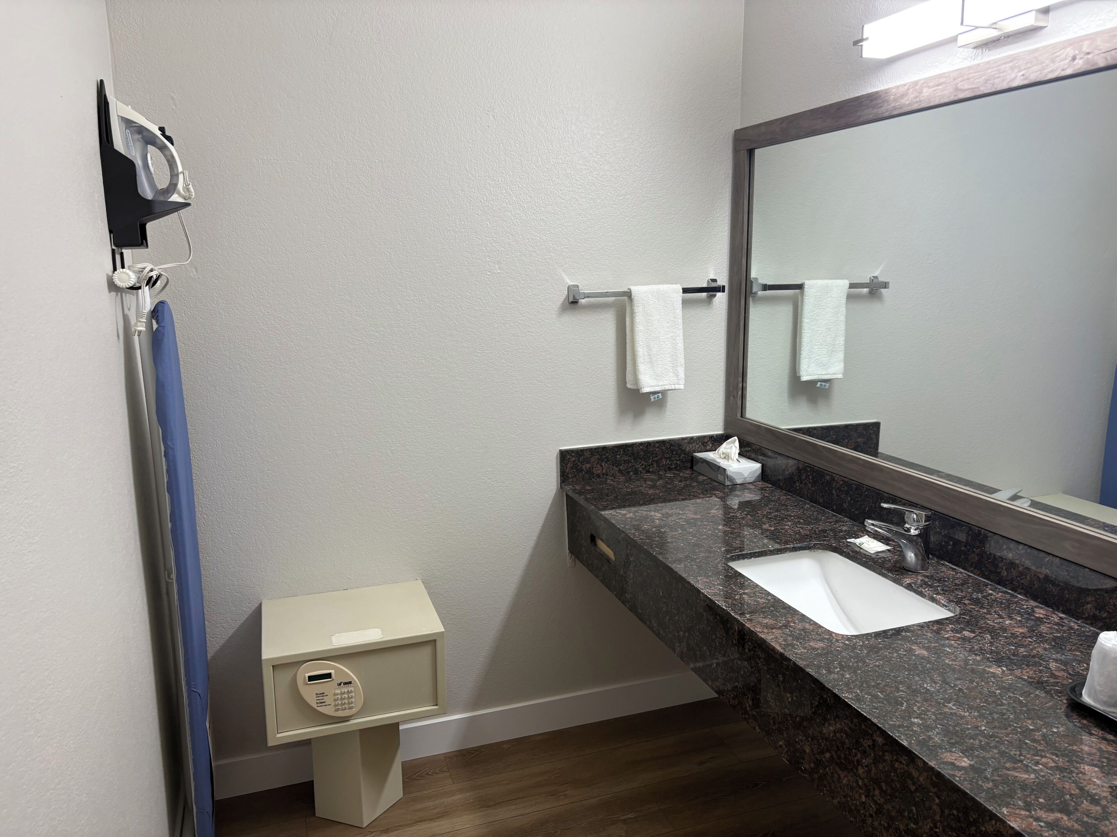 A bathroom with a sink, mirror, towel rack, and a small cabinet with a control panel.