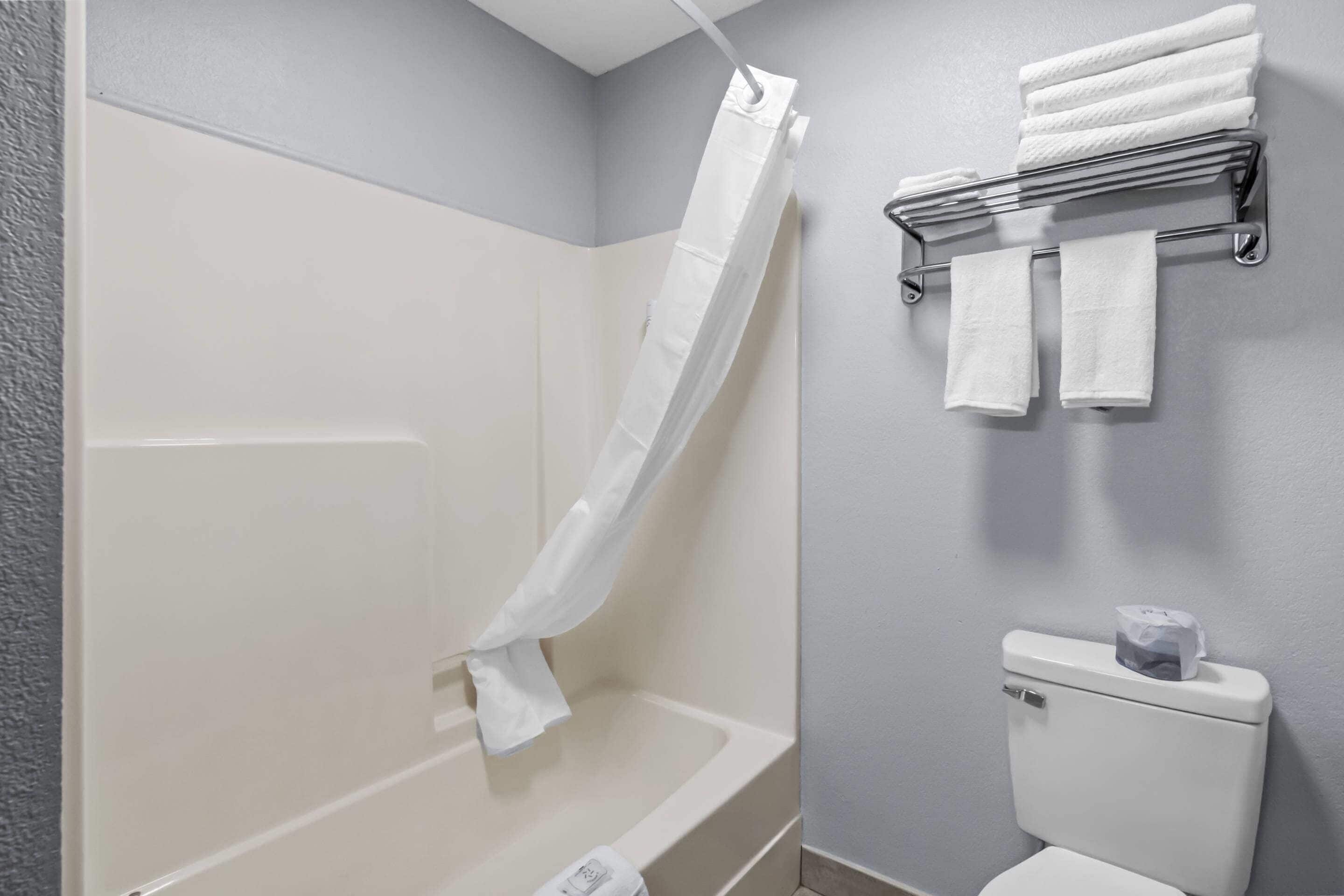 A bathroom with a bathtub, a shower curtain, a toilet, and a towel rack with towels.